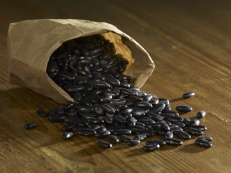 Bag of black beans spilled on wooden surface - SRSF00147