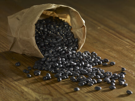 Bag of black beans spilled on wooden surface - SRSF00146
