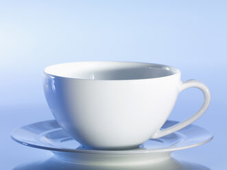 Empty tea cup and saucer against blue background, close-up - SRSF00144