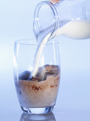 Human hand pouring milk into glass of cocoa, close-up - SRSF00135