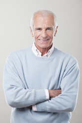 Man standing with arms crossed against gray background, smiling, portrait - CLF00917