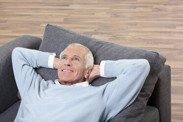 Mann mit Kopf in der Hand auf der Couch liegend, lächelnd - CLF00913