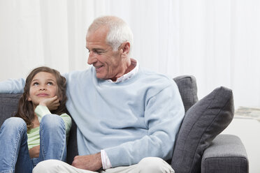 Granddaughter (6-7) and grandfather sitting on couch, smiling - CLF00907