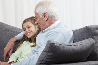 Grandfather whispering into Granddaughter's ear (6-7) , smiling - CLF00903