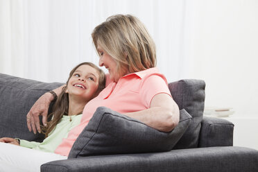 Enkelin (6-7) und Großmutter sitzen lächelnd auf der Couch - CLF00899