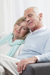 Älteres Paar sitzt auf der Couch, lächelnd, Augen geschlossen - CLF00885