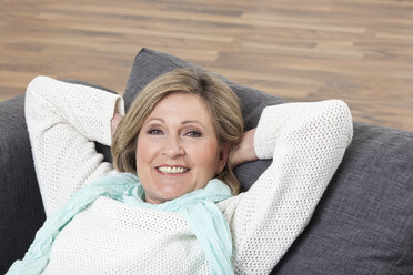 Woman lying with head in hand on couch, smiling, portrait - CLF00879