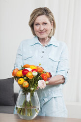 Woman arranging flower into flower vase, smiling, portrait - CLF00877