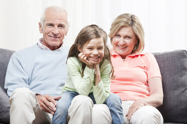 Granddaughter (6-7) sitting on lap of grandparents with head in hand, smiling, portrait - CLF00857