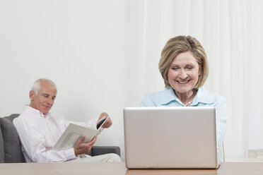 Woman using laptop with man sitting in background - CLF00846
