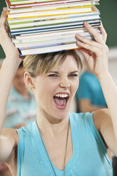 Germany, Emmering, Young woman carrying stack of books with students in background - RNF00324