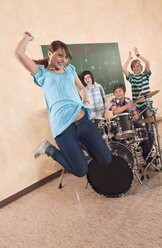 Germany, Emmering, Girl jumping with boys in background playing drums - WESTF14725