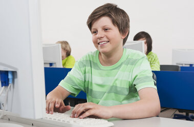 Germany, Emmering, Boy (12-13) smiling and using computer students in background - WESTF14692