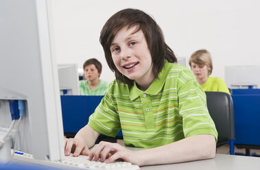 Germany, Emmering, Boy (12-13) smiling and using computer with students in background - WESTF14687