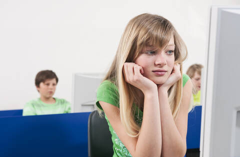 Germany, Emmering, Teenage girl (14-15) with head in hand, boys using computer in background stock photo