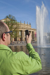 Deutschland, Stuttgart, Älterer Mann, der ein Bild des Opernhauses mit seinem Handy aufnimmt - WDF00746