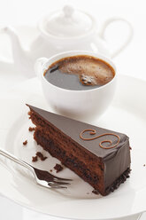 Slice of Sacher cake in plate with coffee cup and kettle in background - 13329CS-U