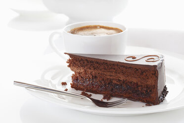 Slice of Sacher cake in plate with coffee cup in background - 13328CS-U