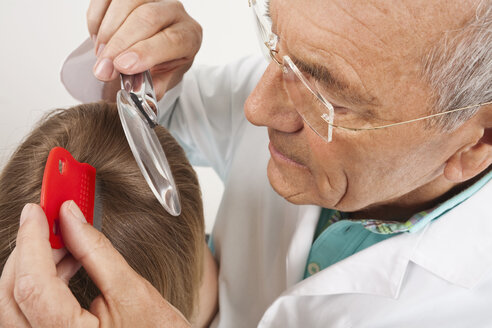 Deutschland, München, Arzt schaut durch ein Vergrößerungsglas in die Haare eines Mädchens (8-9) - WESTF14787