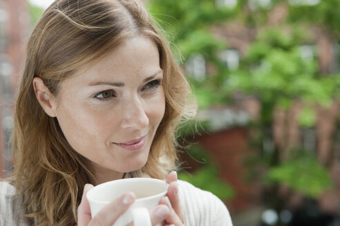 Deutschland, Frau hält Kaffeetasse und schaut weg, lächelnd - WESTF14932