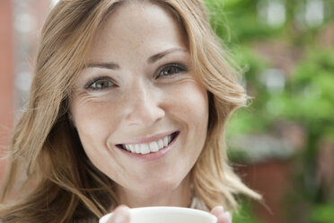 Germany, Woman holding coffee cup, portrait, smiling - WESTF14931