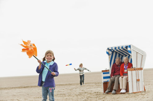 Deutschland, St. Peter-Ording, Nordsee, Kinder (6-9) spielen am Strand und Großeltern sitzen im Strandkorb mit Kapuze - WESTF15084