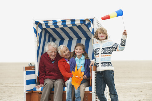Deutschland, St. Peter-Ording, Nordsee, Großeltern mit Kindern (6-9) sitzen im Strandkorb mit Kapuze - WESTF15083