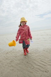 Germany, North Sea, St.Peter-Ording, Girl (6-7) holding bucket and spade walking on beach - WESTF15048