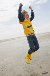 Deutschland, St.Peter-Ording, Nordsee, Junge (8-9) in Regenjacke springt am Strand - WESTF15042