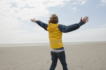 Germany, St.Peter-Ording, North Sea, Boy (8-9) in rain coat standing on beach, arms up - WESTF15039