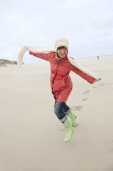 Germany, St Peter-Ording, North sea, Woman having fun in sand dunes, smiling, portrait - WESTF14993