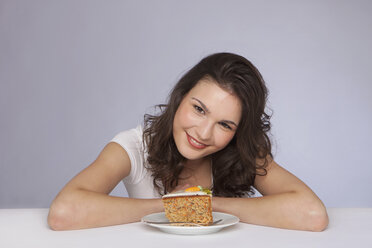 Young woman sitting with plate of cake, smiling, portait - SKF00236