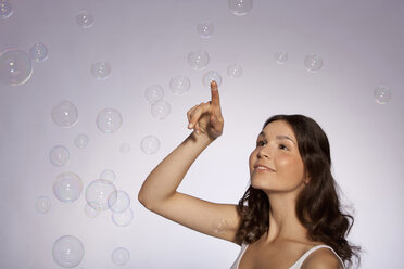 Young woman touching soap bubble, smiling - SKF00216