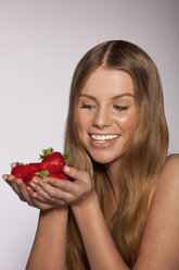 Junge Frau hält eine Handvoll Erdbeeren in der Hand, lächelnd, Nahaufnahme - SKF00194