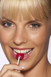 Portrait of young woman eating lollipop, smiling, close up - SKF00164