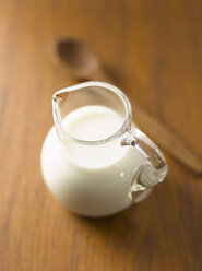 Close up of milk in pitcher and wood spoon - KSWF000567