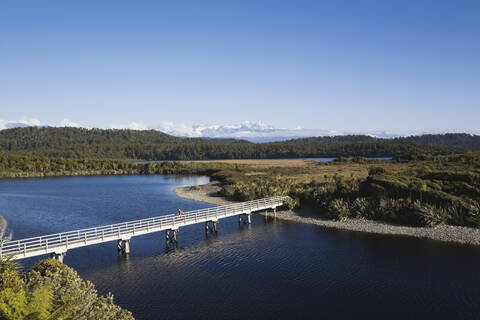 Neuseeland, Südinsel, Westküste, Mann überquert Brücke mit Bergen im Hintergrund, lizenzfreies Stockfoto