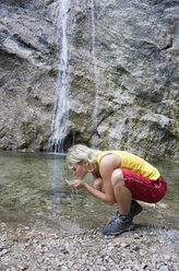 Österreich, Salzkammergut, Weissenbachtal, Junge Frau trinkt Wasser aus Wasserfall - WWF001529