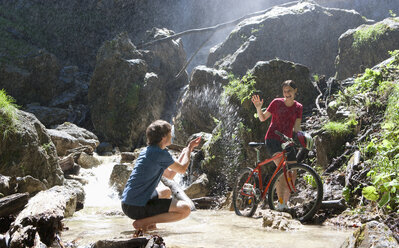 Österreich, Salzkammergut, Mondsee, Junges Paar mit Fahrrad und Wasserfall im Hintergrund - WWF001524