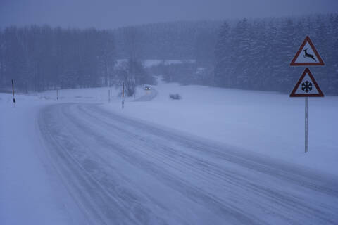 Deutschland, Bayern, Mörlbach, Blick auf fahrendes Auto auf schneebedeckter Landstraße mit Hinweisschild, lizenzfreies Stockfoto