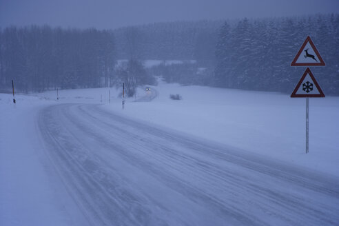Deutschland, Bayern, Mörlbach, Blick auf fahrendes Auto auf schneebedeckter Landstraße mit Hinweisschild - TCF001341