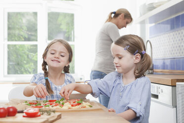 Deutschland, München, Mädchen (4-7) bei der Essenszubereitung in der Küche, Mutter steht im Hintergrund - RBF000309