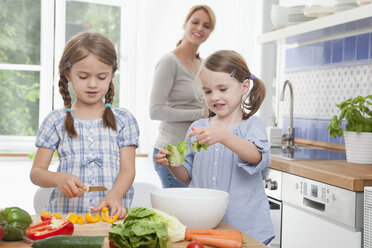 Germany, Munich, Girls (4-7) chopping vegetables in kitchen, mother standing in background - RBF000297