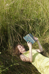 Germany, Munich, Woman lying on grass and reading book - LDF000888