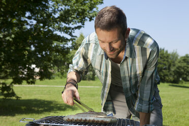 Germany, Munich, Man preparing sausages on brabecue grill - LDF000872