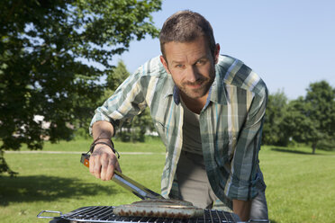 Germany, Munich, Man preparing sausages on brabecue grill - LDF000871