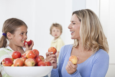 Mother and daughter eating apple with son in background - LDF000834