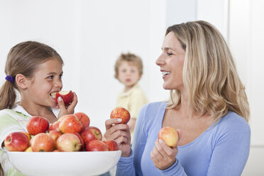 Mutter und Tochter essen Apfel mit Sohn im Hintergrund - LDF000834