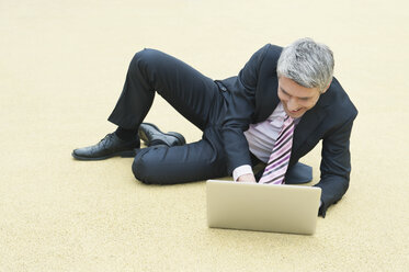 Deutschland, Hamburg, Geschäftsmann sitzt auf dem Boden und benutzt Laptop - WESTF015282