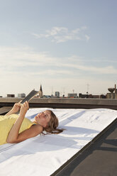 Germany, Bavaria, Munich, Young woman eading a book on a rooftop - SKF000392